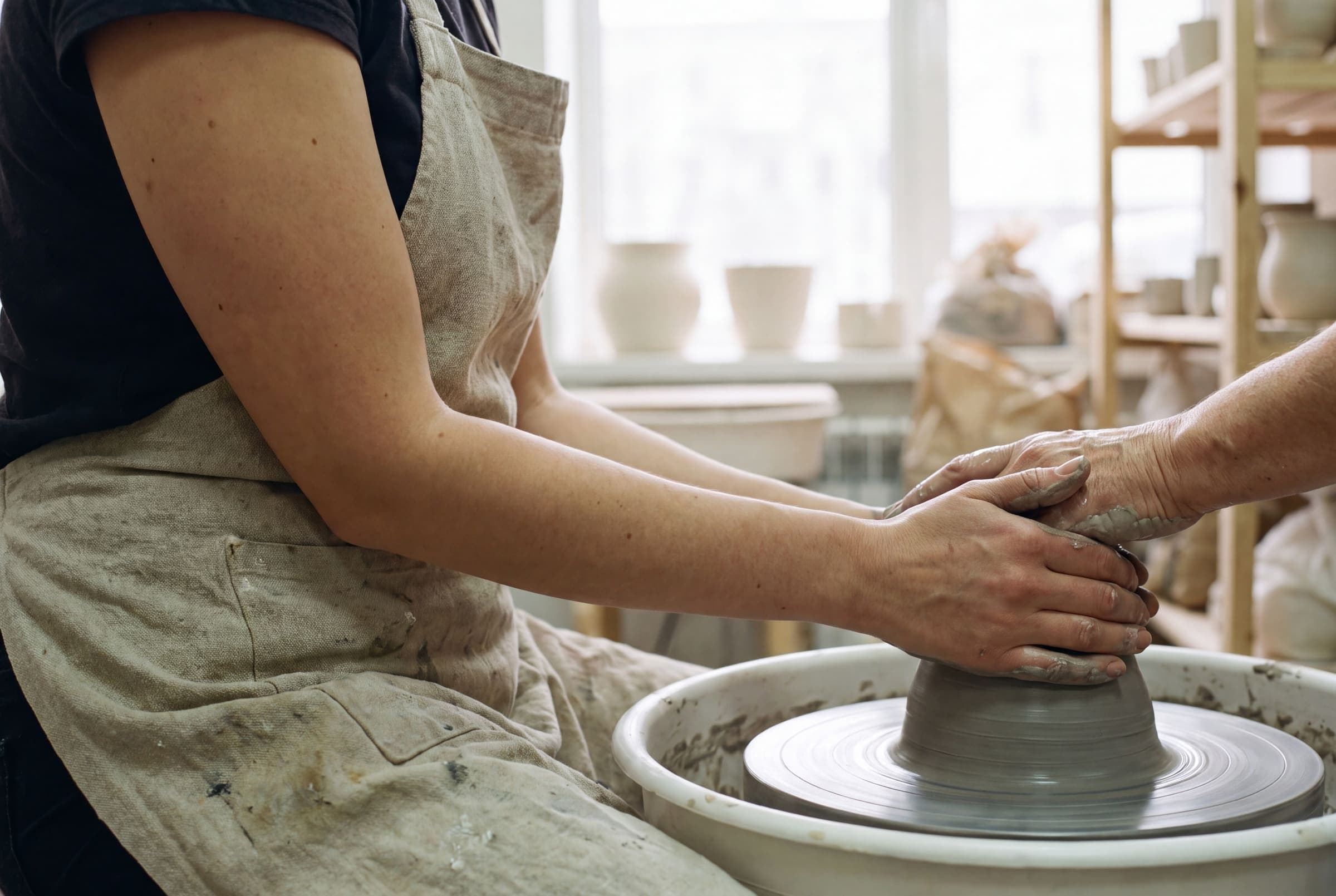 Two hands braced against wet clay, forearms resting on the wheel tray
